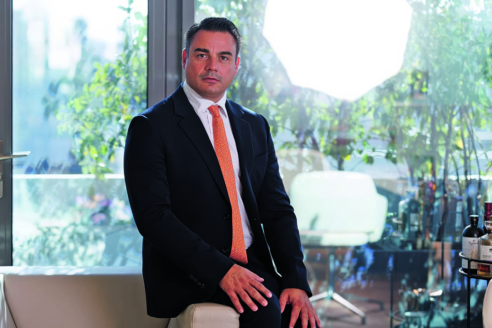 Man in a dark suit with pink tie sitting on the edge of a chair